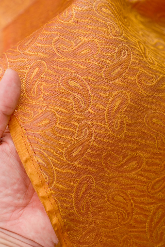 〔1m単位切り売り〕インドの伝統模様布 - 橙地にペイズリー〔幅112cm〕 4 - 端のほうを手で持ってみました。適度な薄手の生地で、使いみちに広がりがあります。